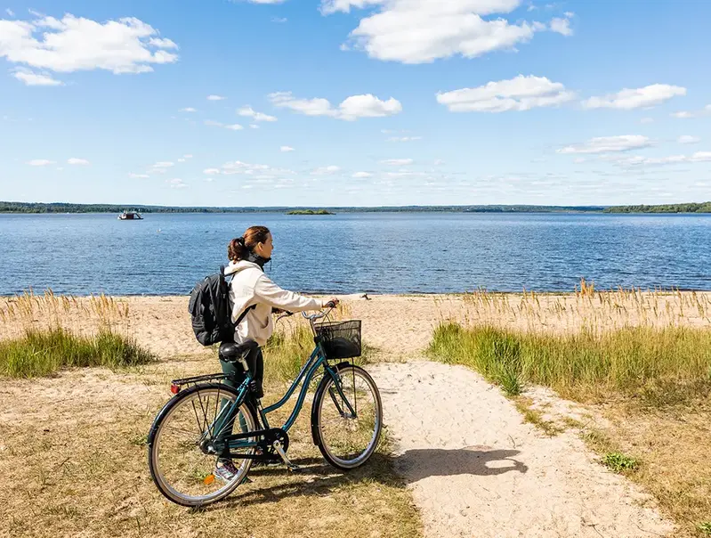 Kvinna som leder en cykel på stranden vid Finjasjön.