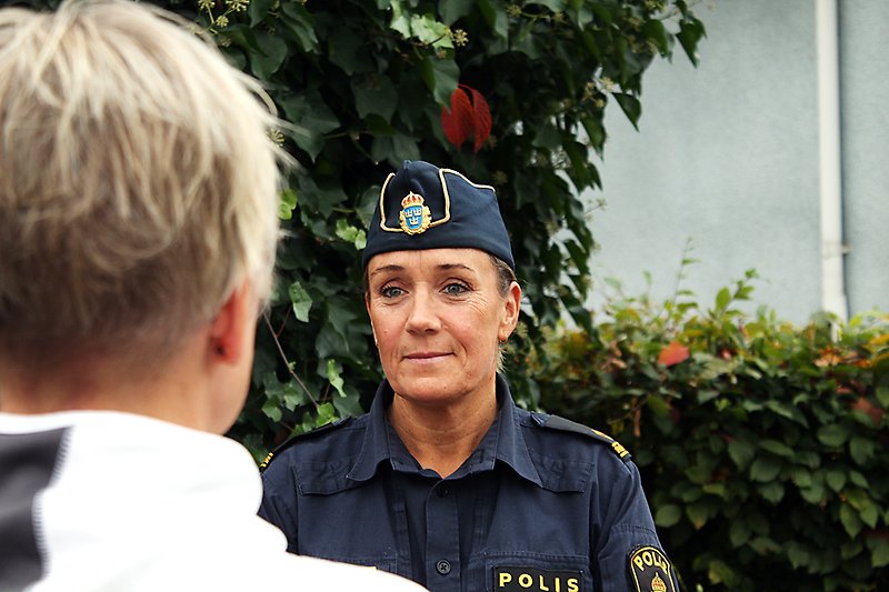 Kvinnlig polis som står vid en grön buske.