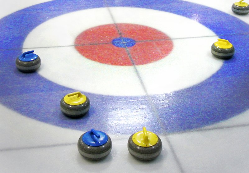 Spelplan för curling och flera curlingstenar ligger på isen.