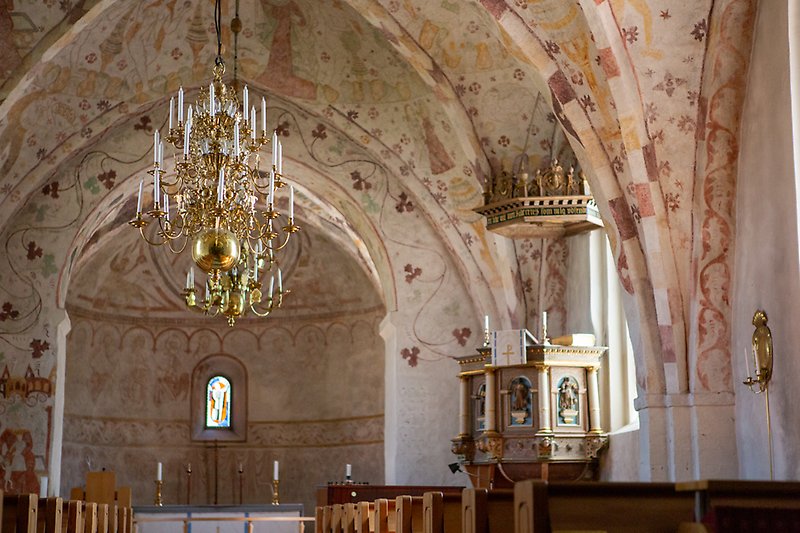 Interiörsbild i kyrka där man ser en guldkrona hänga ner från ett målat tak med talarstolen i bakgrunden.