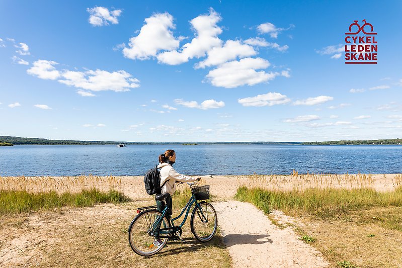 Tjej med cykel står vid strandkanten av en sjö