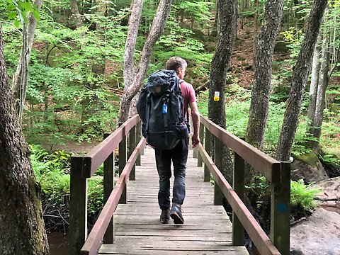 En man på vandring med ryggsäck går över en bro.