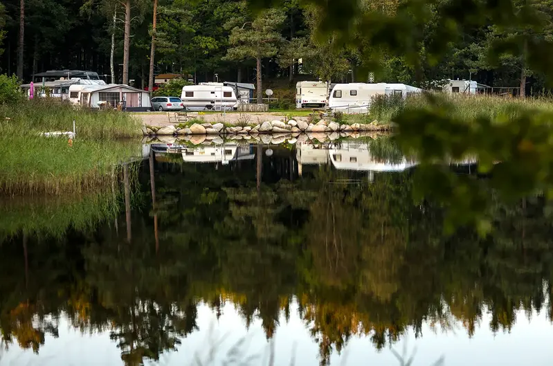 En camping med parkerade husvagnar och husbilar intill en sjö.
